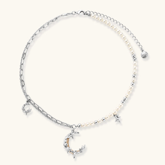 Silver-toned crescent moon pendant with star accents on pearl and chain necklace against white background.