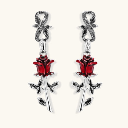 Gothic dangle earrings featuring silver serpent hooks with red enamel roses and metallic stems on white background.