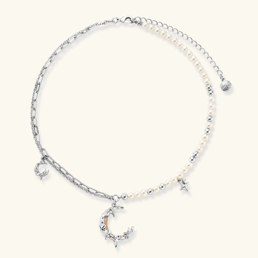 Silver-toned crescent moon pendant with star accents on pearl and chain necklace against white background.