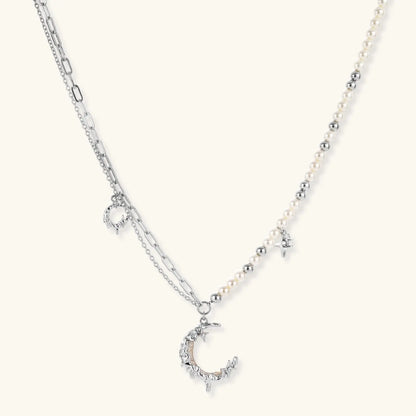 Silver-toned crescent moon pendant with star accents on pearl and chain necklace against white background.
