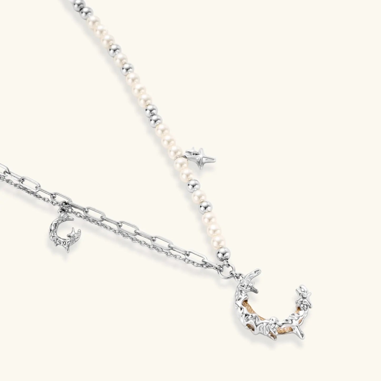 Silver-toned crescent moon pendant with star accents on pearl and chain necklace against white background.
