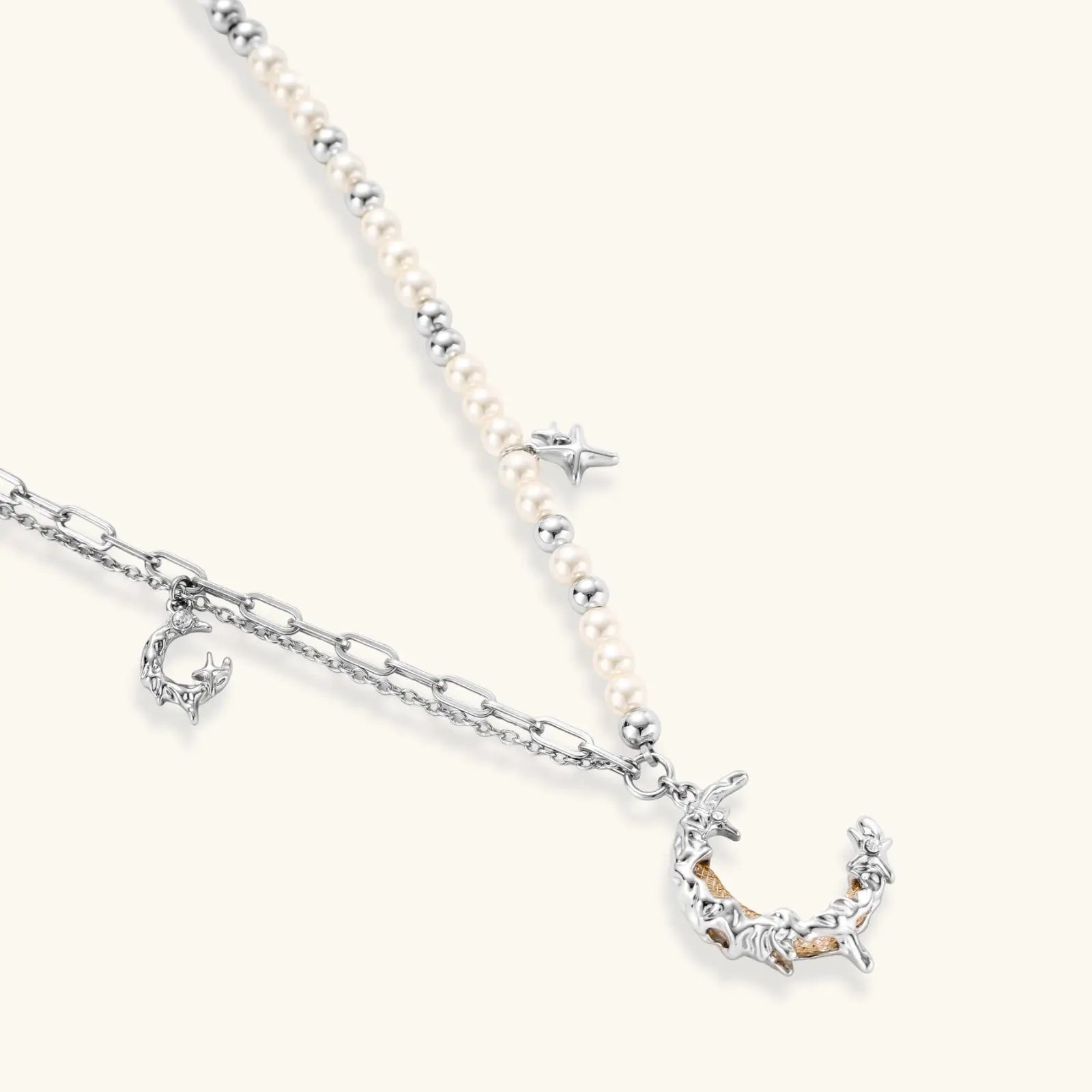 Silver-toned crescent moon pendant with star accents on pearl and chain necklace against white background.