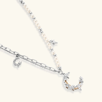 Silver-toned crescent moon pendant with star accents on pearl and chain necklace against white background.