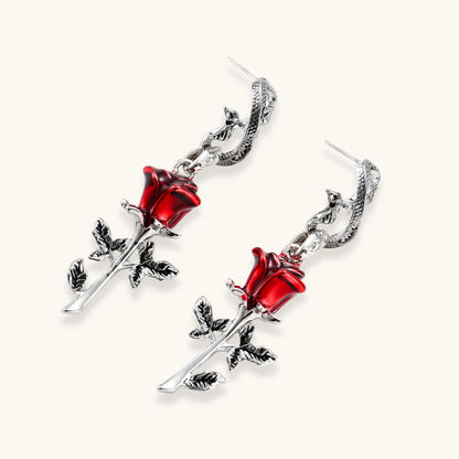 Gothic dangle earrings featuring silver serpent hooks with red enamel roses and metallic stems on white background.