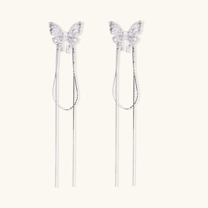Pair of silver threader earrings with crystal butterfly tops and long chain drops on cream background.