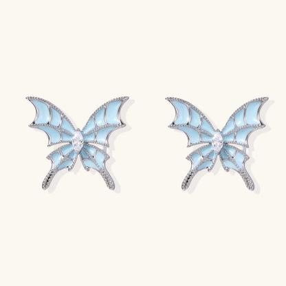 Long silver-tone earrings with powder blue enamel butterfly studs and flowing chain tassels on cream background