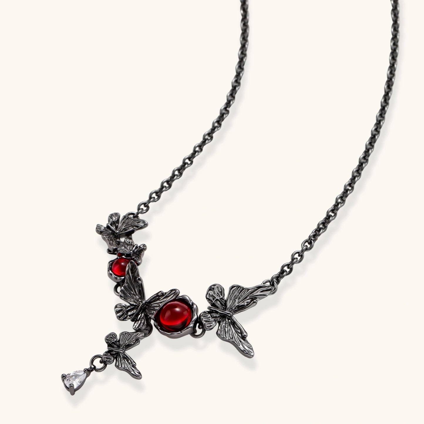 Dark oxidized metal necklace featuring red resin stones set in decorative leaf vine design with crystal drop pendant.