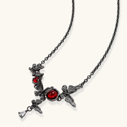 Dark oxidized metal necklace featuring red resin stones set in decorative leaf vine design with crystal drop pendant.