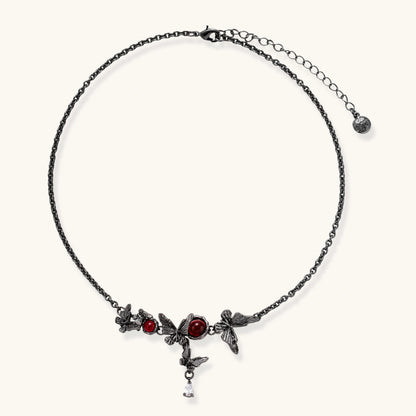 Dark oxidized metal necklace featuring red resin stones set in decorative leaf vine design with crystal drop pendant.