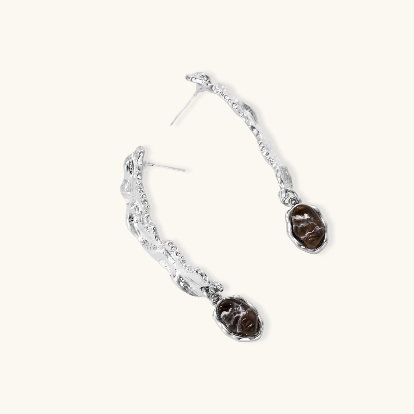 Silver-toned twisted metal earrings with dark brown oval resin stones dangling from sculptural posts on white background.