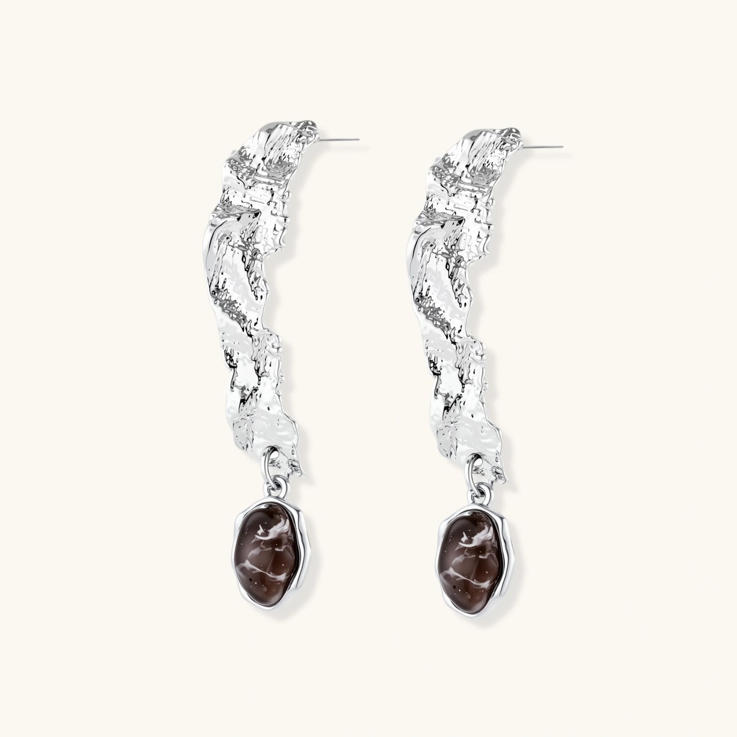 Silver-toned twisted metal earrings with dark brown oval resin stones dangling from sculptural posts on white background.