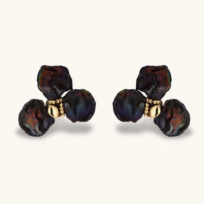 Dark iridescent baroque pearls arranged in flower pattern with 18K gold-plated center on cream background.